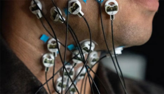 Close-up of a person’s neck and lower face with multiple small circular sensors attached to the skin, each connected by thin wires.