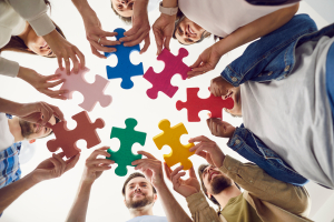 A view of happy smiling people putting together pieces of different colors of puzzles together.