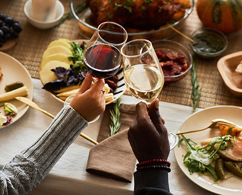 A cozy dinner table with candles, shared wine toast, and a spread of roasted meat, cheese and fruit.