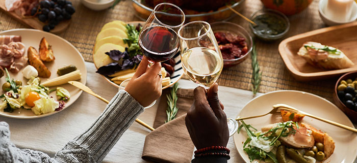 A cozy dinner table with candles, shared wine toast, and a spread of roasted meat, cheese and fruit.
