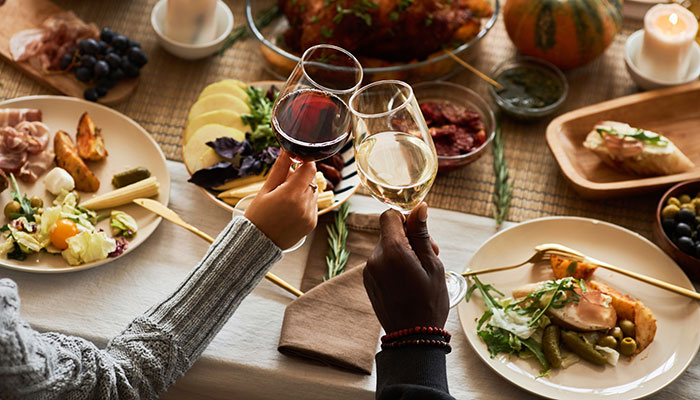 A cozy dinner table with candles, shared wine toast, and a spread of roasted meat, cheese and fruit.