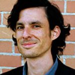 Head shot of smiling man with quite long dark hair and dark blue shirt